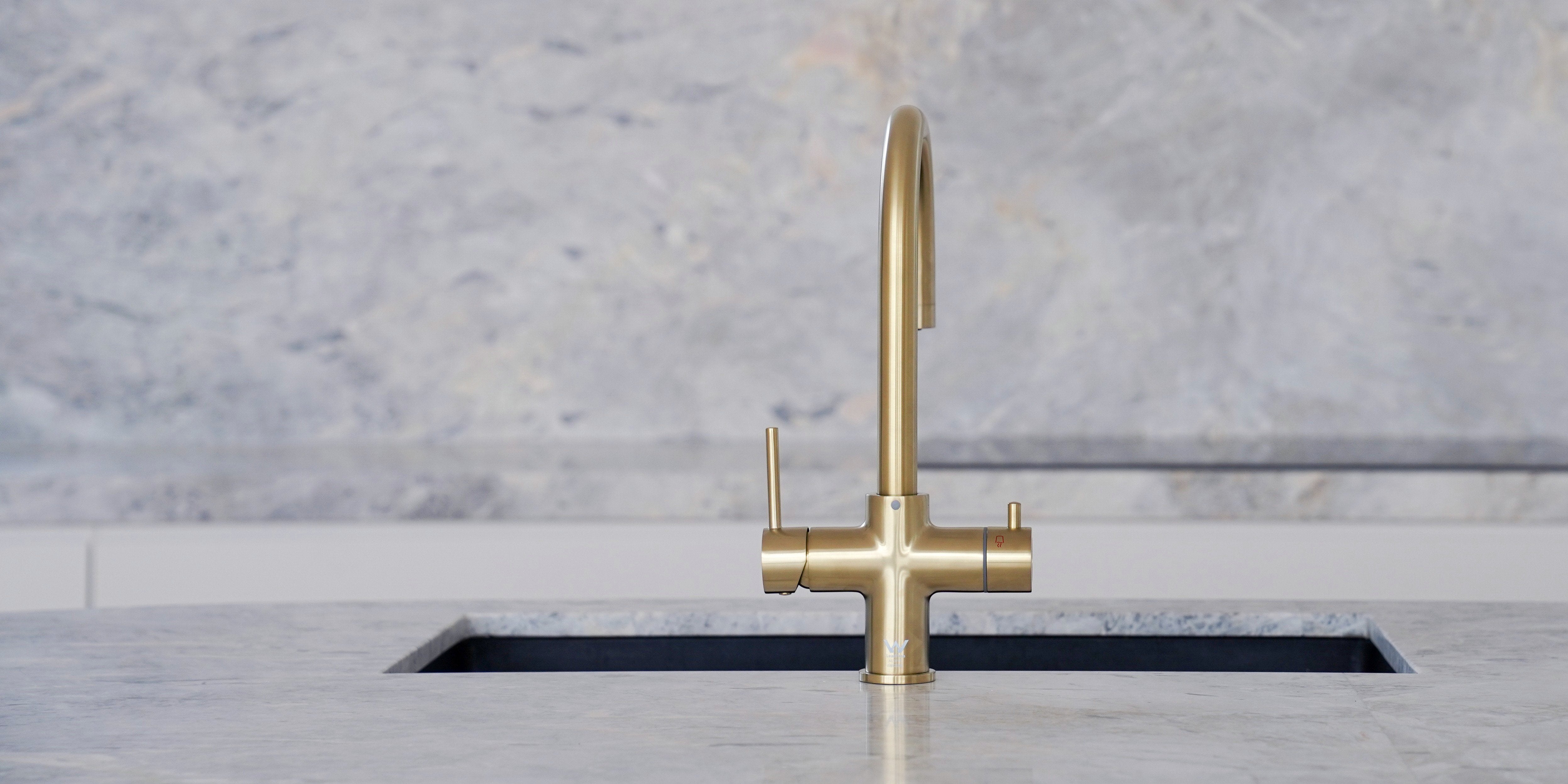 Brushed gold 4-in-1 hot and cold water tap installed in a modern marble kitchen, showcasing an elegant and functional filtered water dispenser for contemporary home design.