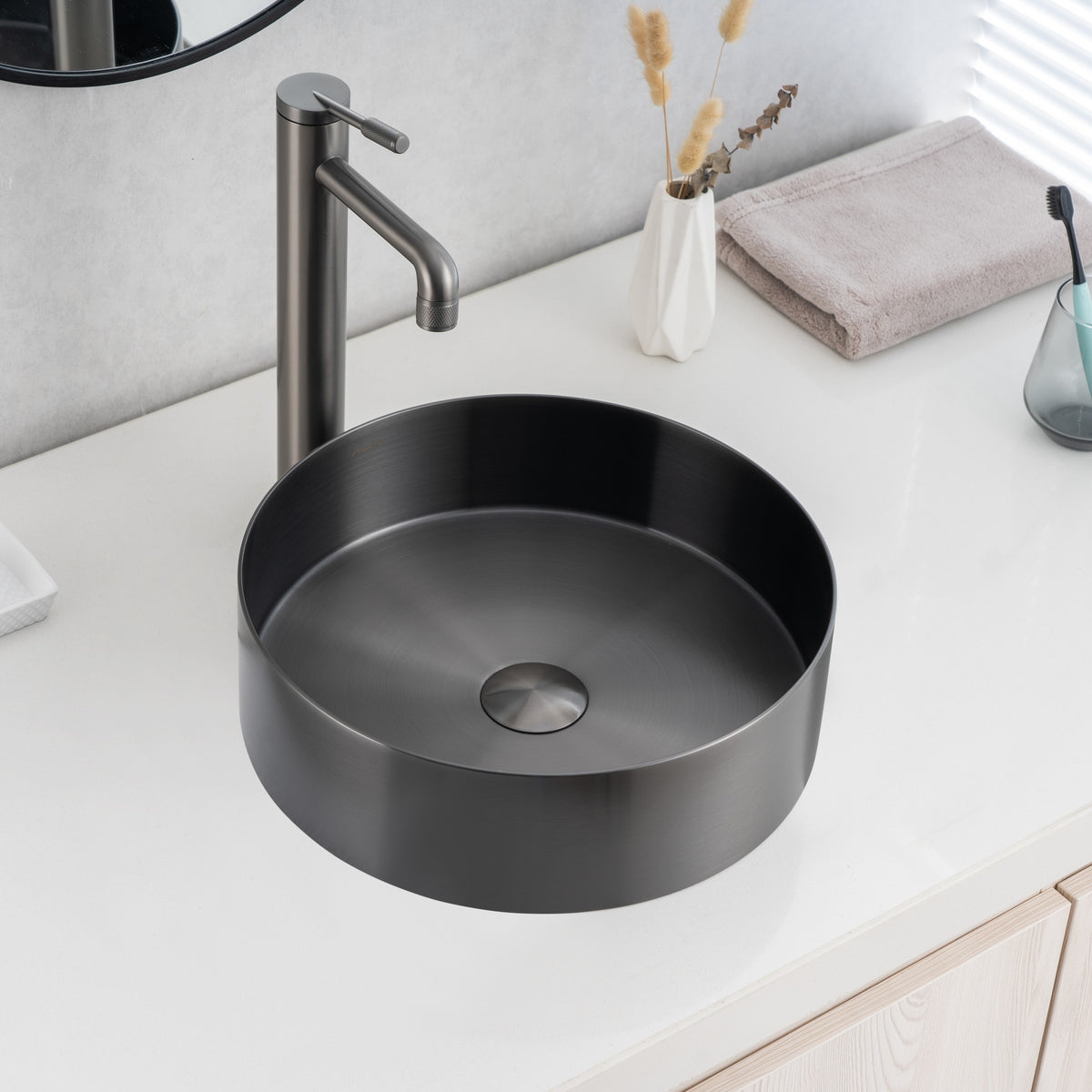 Real image of installed ALIA gunmetal grey round basin highlighting modern above-counter placement and reflective surface. Black round sink with silver faucet on a white countertop.